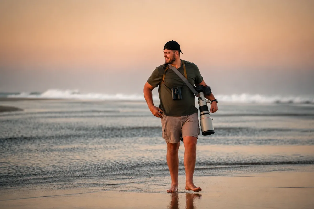 Christo Swart walking barefoot along the beach at sunset with binoculars and a long telephoto lens