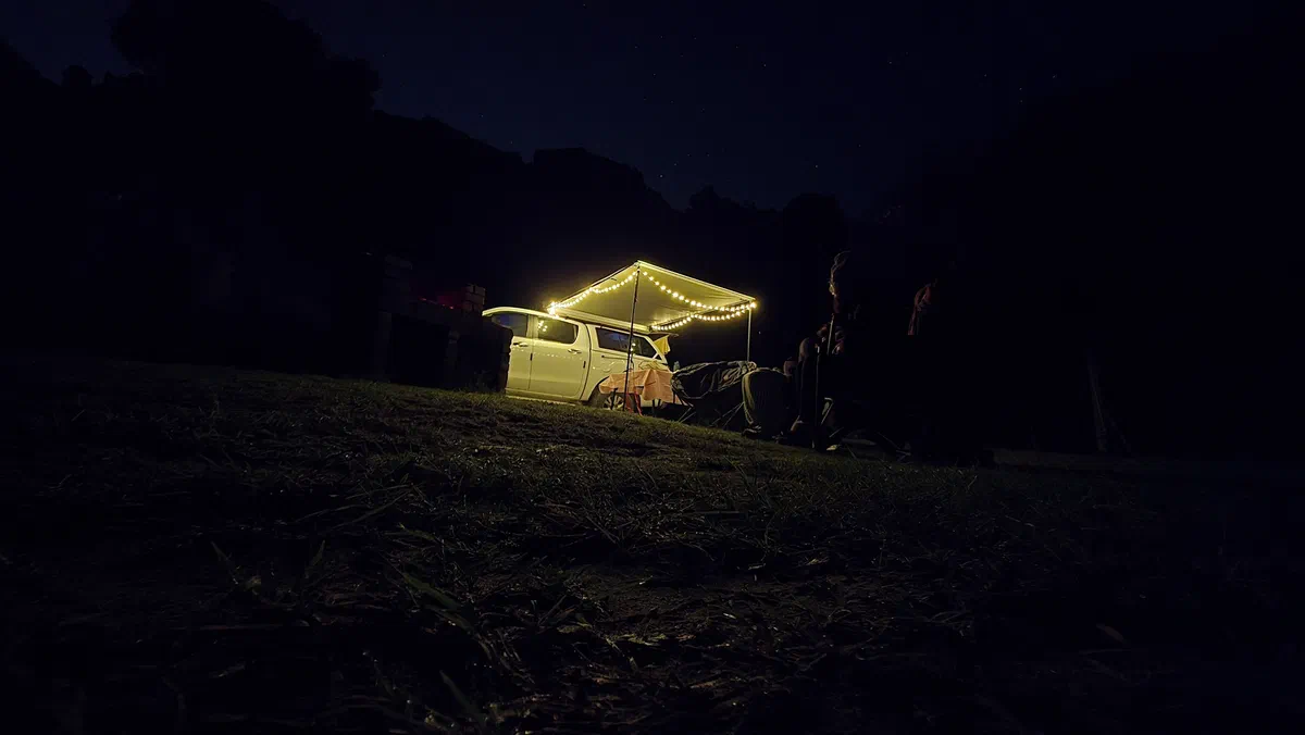 Camp at night, with the vehicle's awning lit by fairy lights