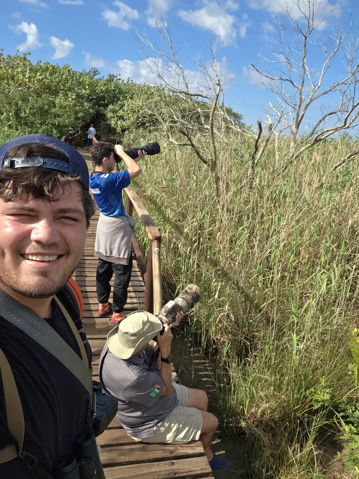 A selfie on a reed-lined boardwalk, with guests photographing behind