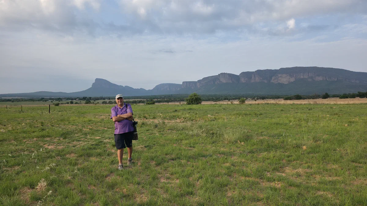 A guest with binoculars in green grassland below sandstone cliffs