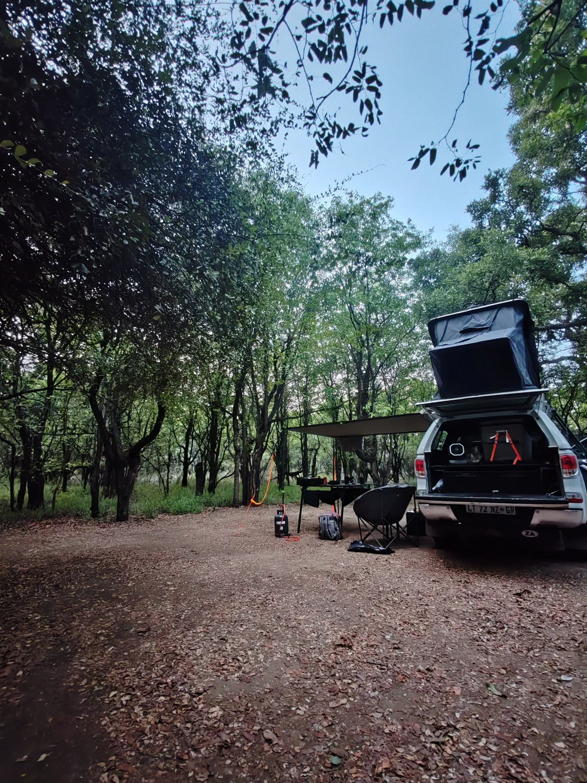 The vehicle with its rooftop tent and awning set up at a shaded camp