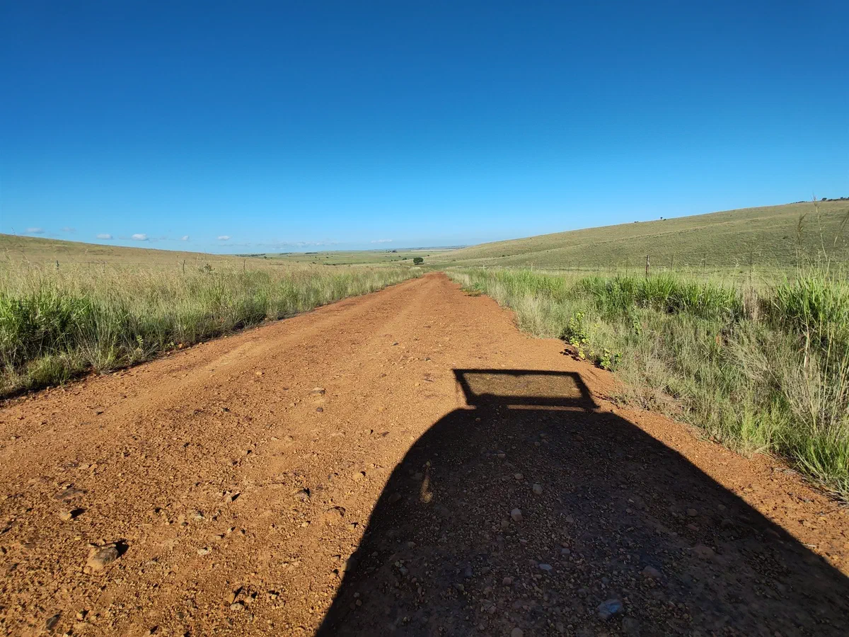 A red dirt road through grassland, with the shadow of the vehicle in the foreground