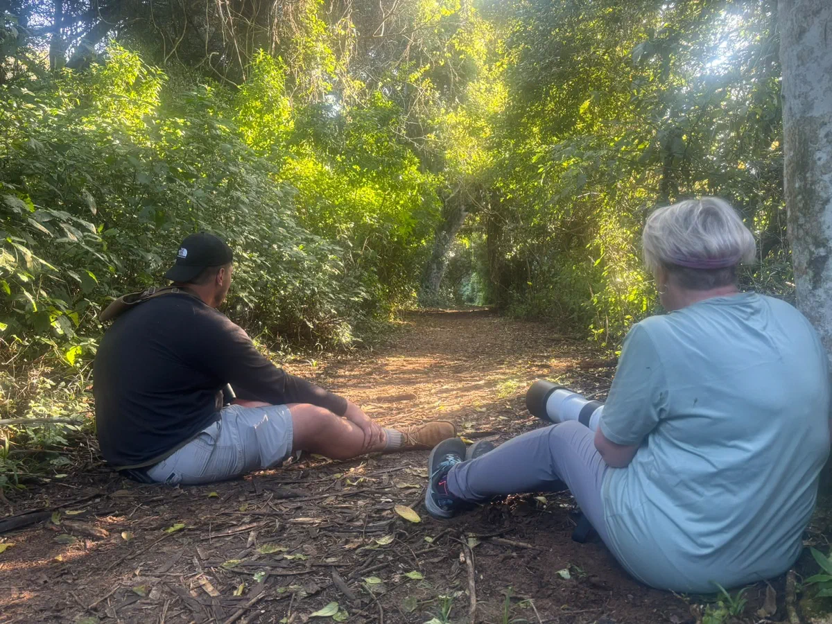 Two guests resting against a tree on a forest path